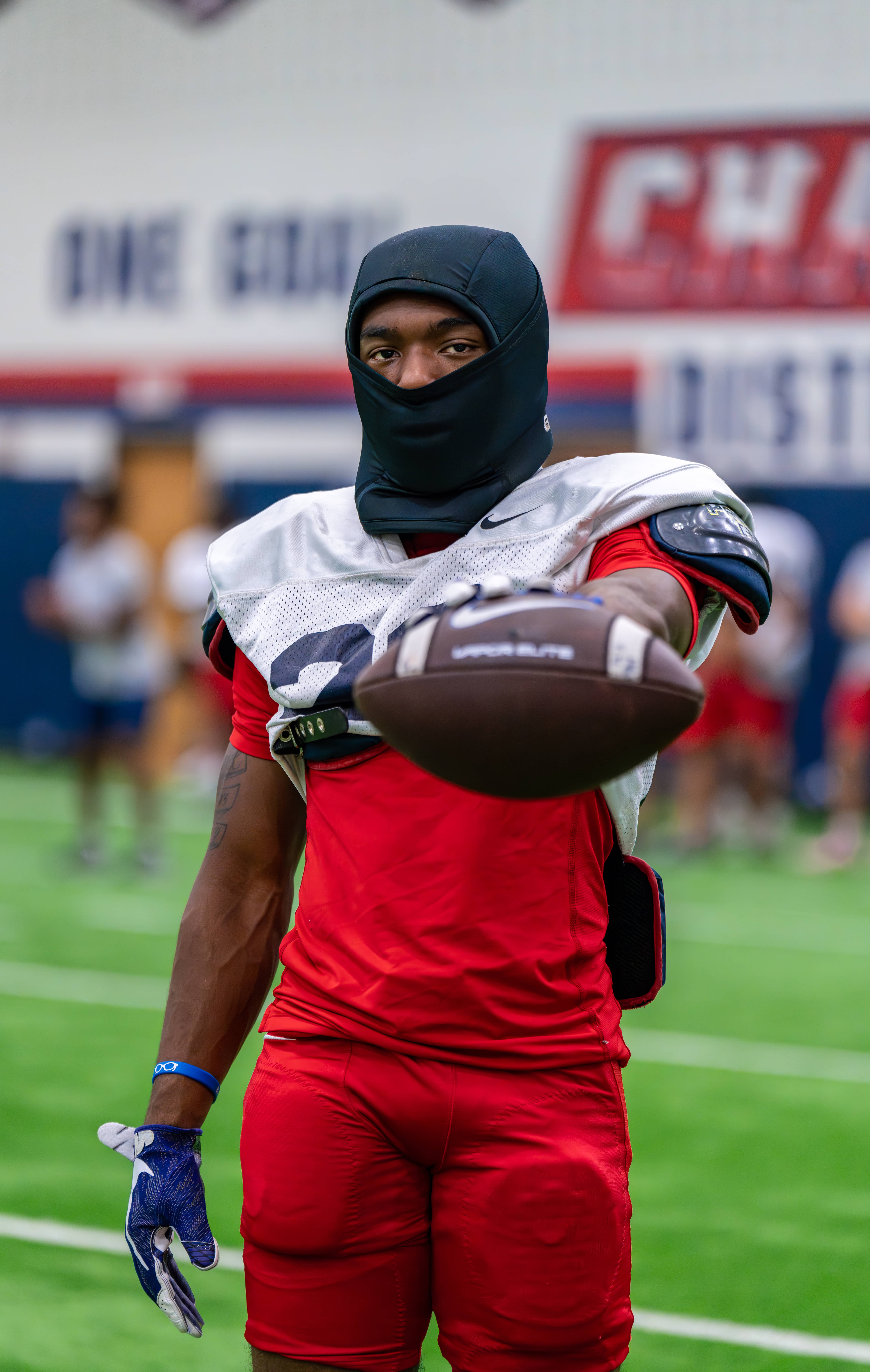 A man in a mask holds a football, showcasing a blend of sports and safety in a dynamic outdoor setting.