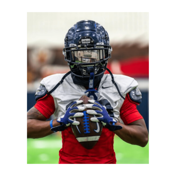 A football player in a helmet confidently holds a football, ready for action on the field.