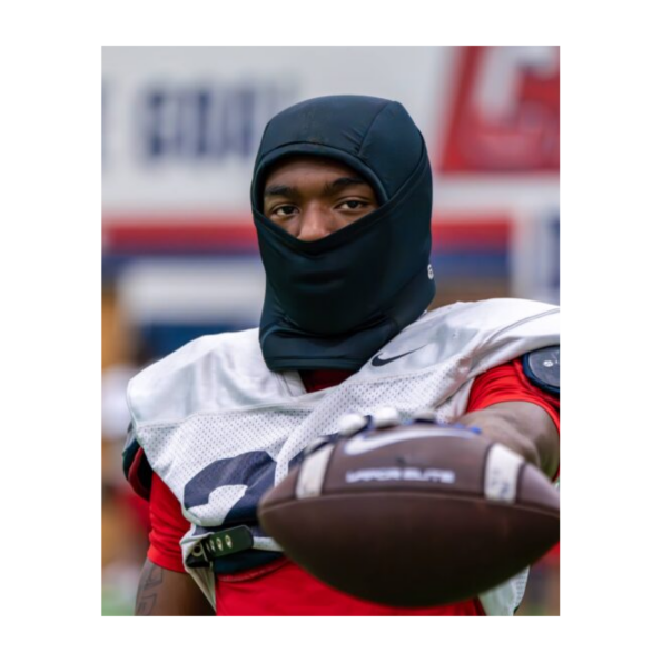 A man in a mask holds a football, showcasing a blend of sports and safety in a dynamic outdoor setting.